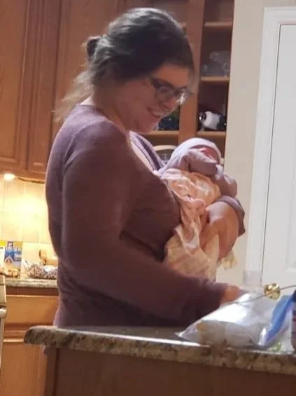 A woman holding a newborn baby in a kitchen.