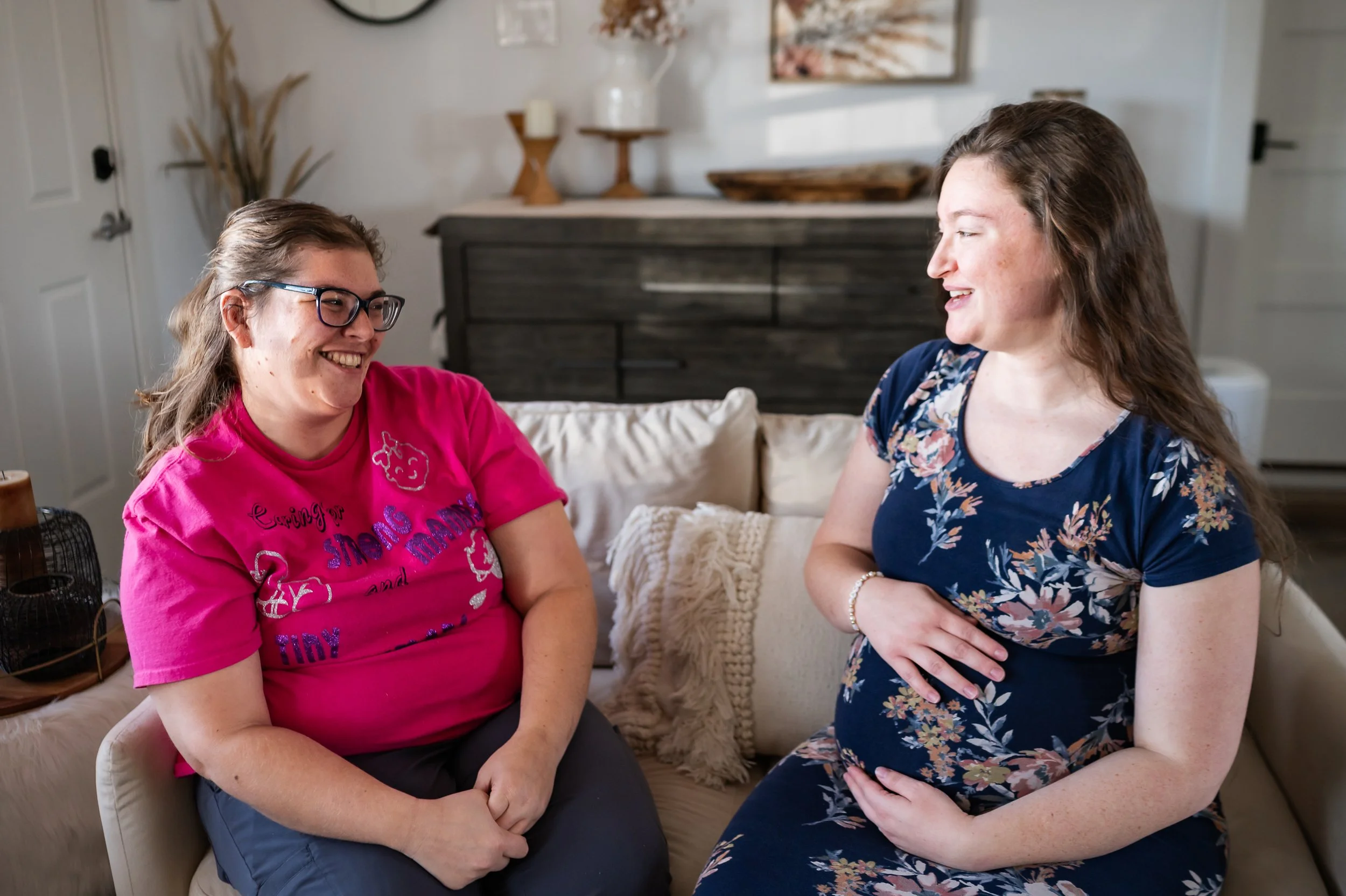 "Doula Melanie Powell sitting on the couch smiling as she talks to a pregnant mom