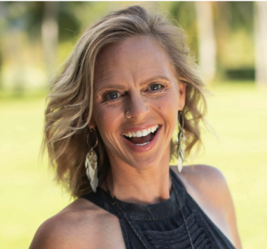 A woman smiling outdoors with earrings and a sleeveless top.