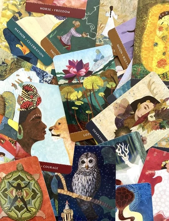 A colorful assortment of oracle or trading cards featuring various artistic images, including a woman with a lion, an owl in a tree, lotus flowers, a woman with a butterfly, a horse, and celestial themes.