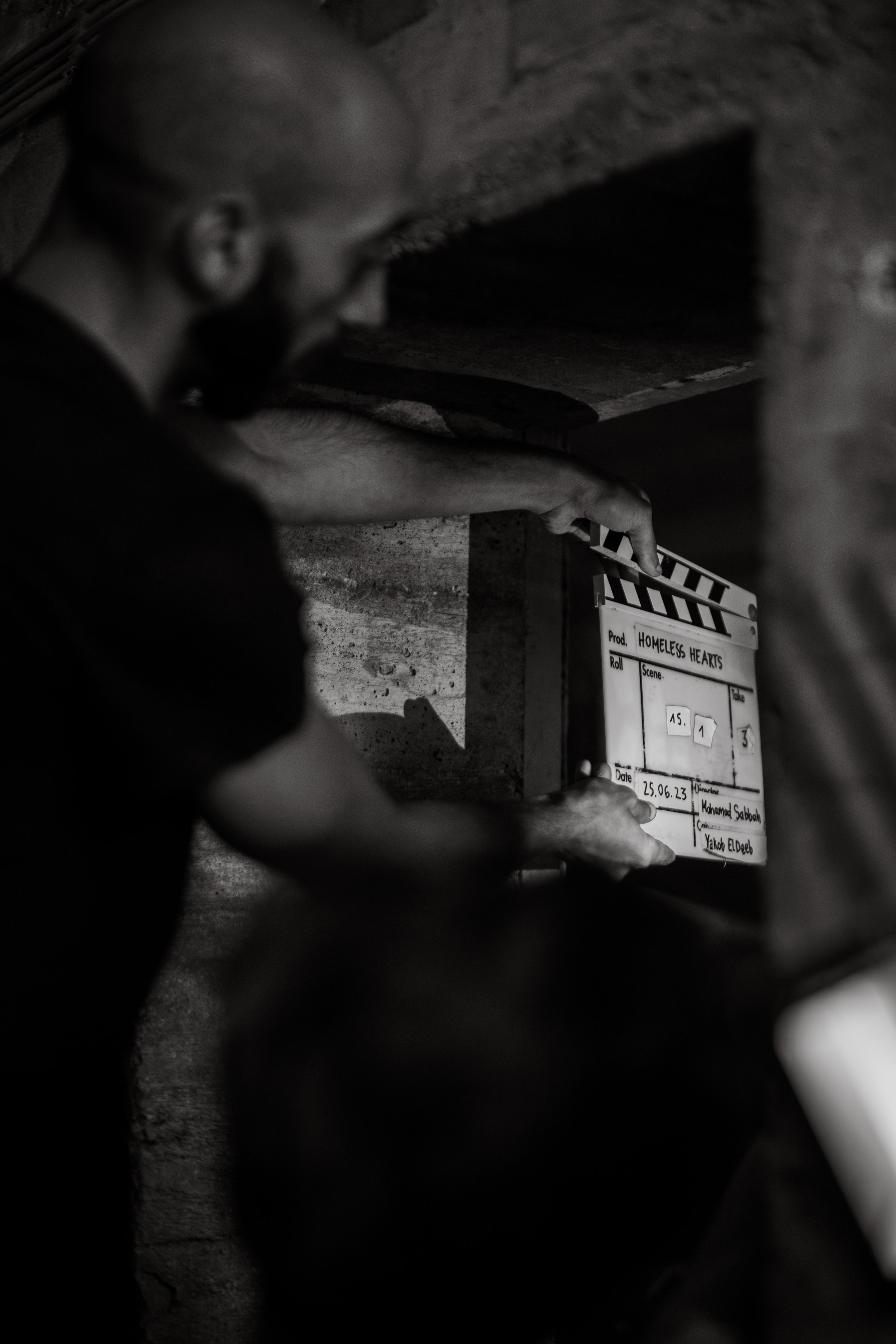 Schwarz-Weiß-Aufnahme von einem Mann, der eine Filmklappe in einem dunklen Raum hält.