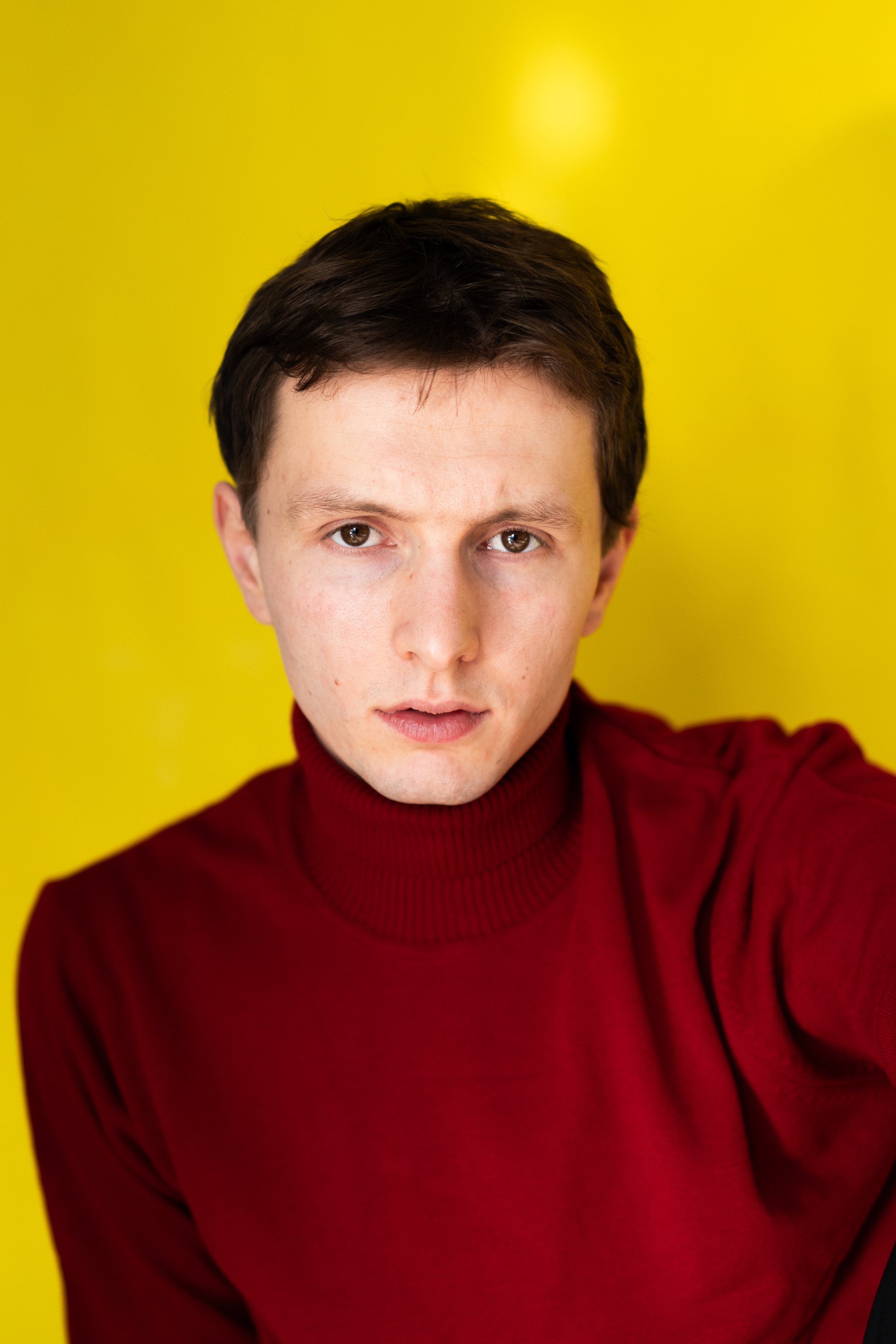 Junge Mann in rotem Pullover vor gelbem Hintergrund, macht Selfie.