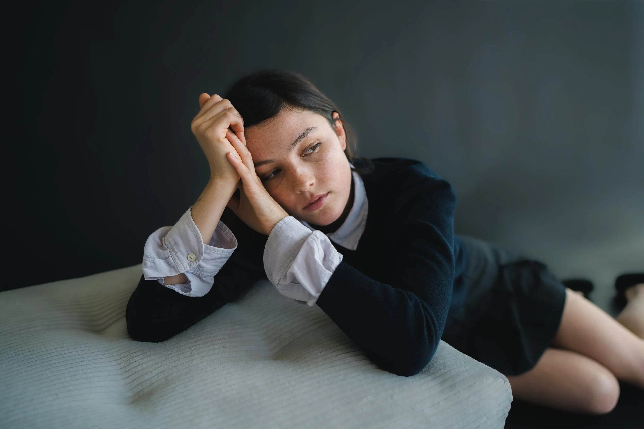Eine junge Frau liegt auf einem Sofa, schaut nachdenklich und wirkt müde oder gelangweilt.
