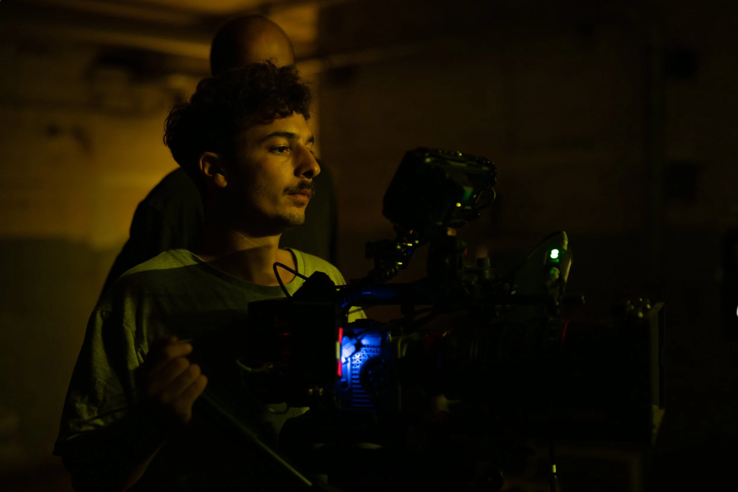 Ein junger Mann bedient eine professionelle Filmkamera in einem dunklen Raum.