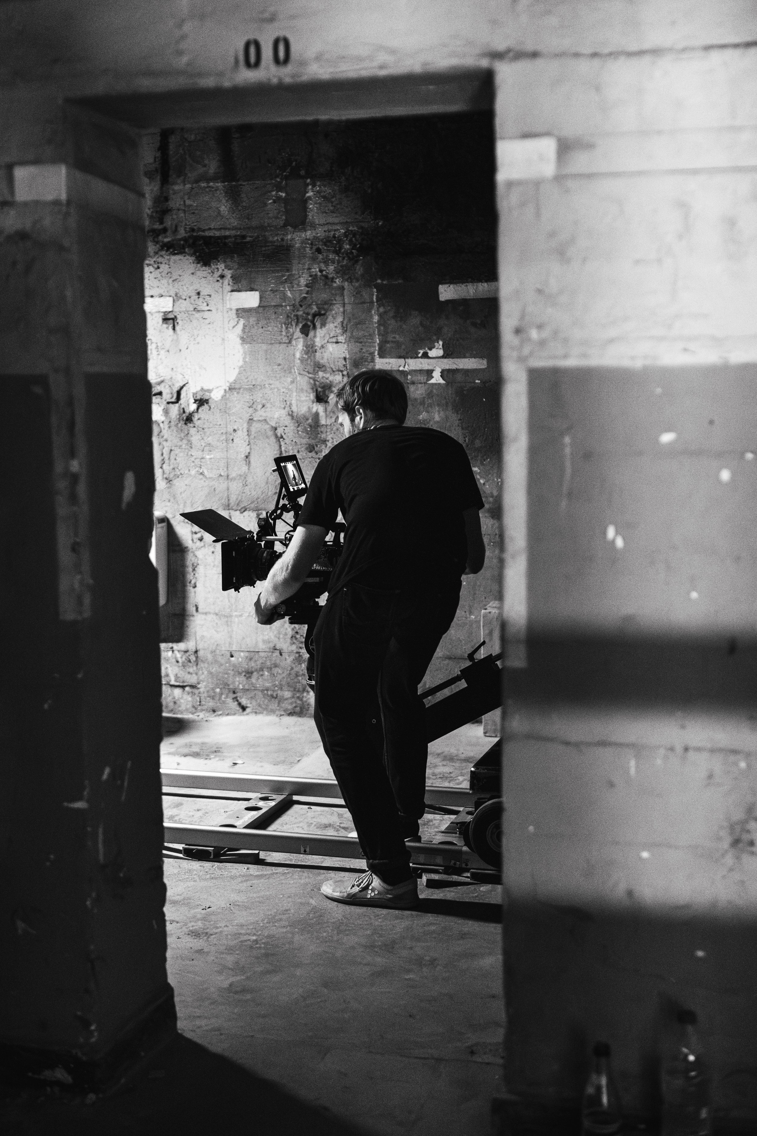 Ein Mann filmt mit einer Kamera in einem alten, verschmutzten Raum, der für einen Film- oder Fotoshooting-Set vorbereitet wird.