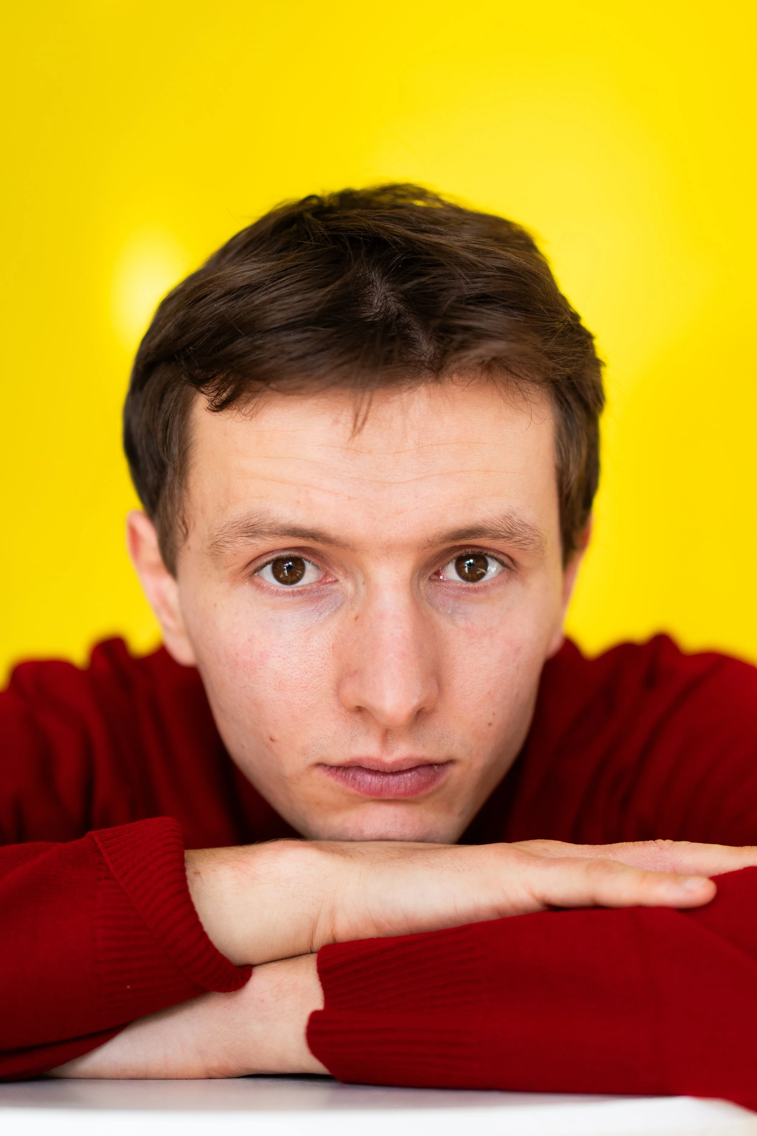 Junger Mann mit braunen Haaren, in rotem Pullover, Blick direkt in die Kamera, mit gelbem Hintergrund.