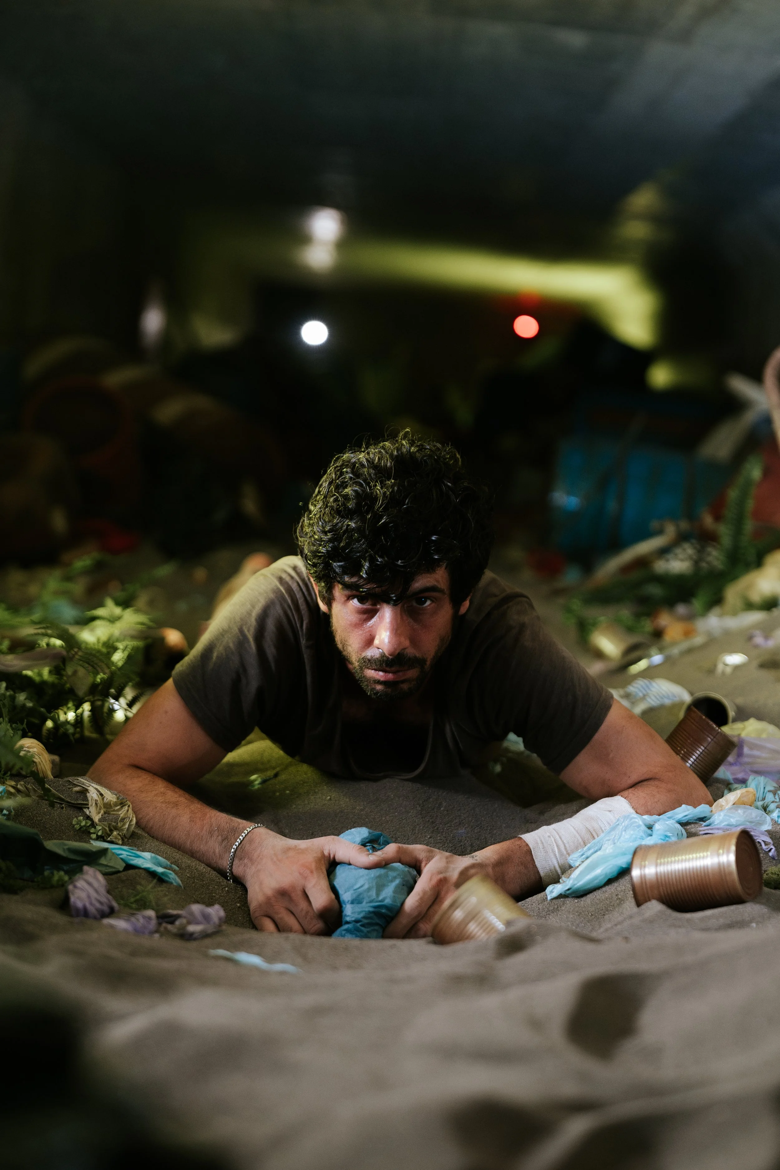 Mann liegt auf dem Bauch in einer Müllkippe, umgeben von Abfall und Plastik, schaut direkt in die Kamera.