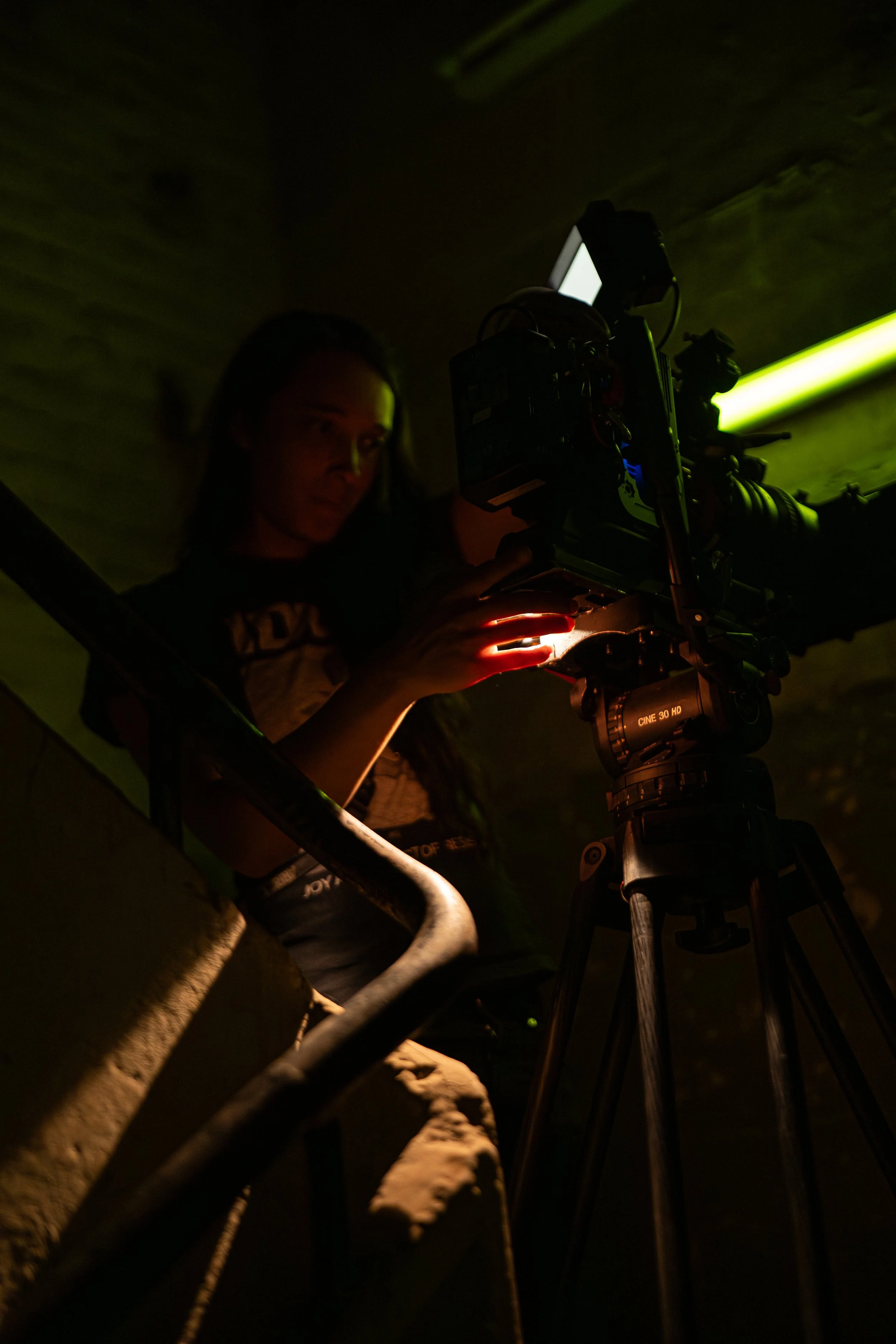 Junge Frau filmt mit professioneller Kamera in dunklem Raum, grüner Lichtstrahl an der Wand