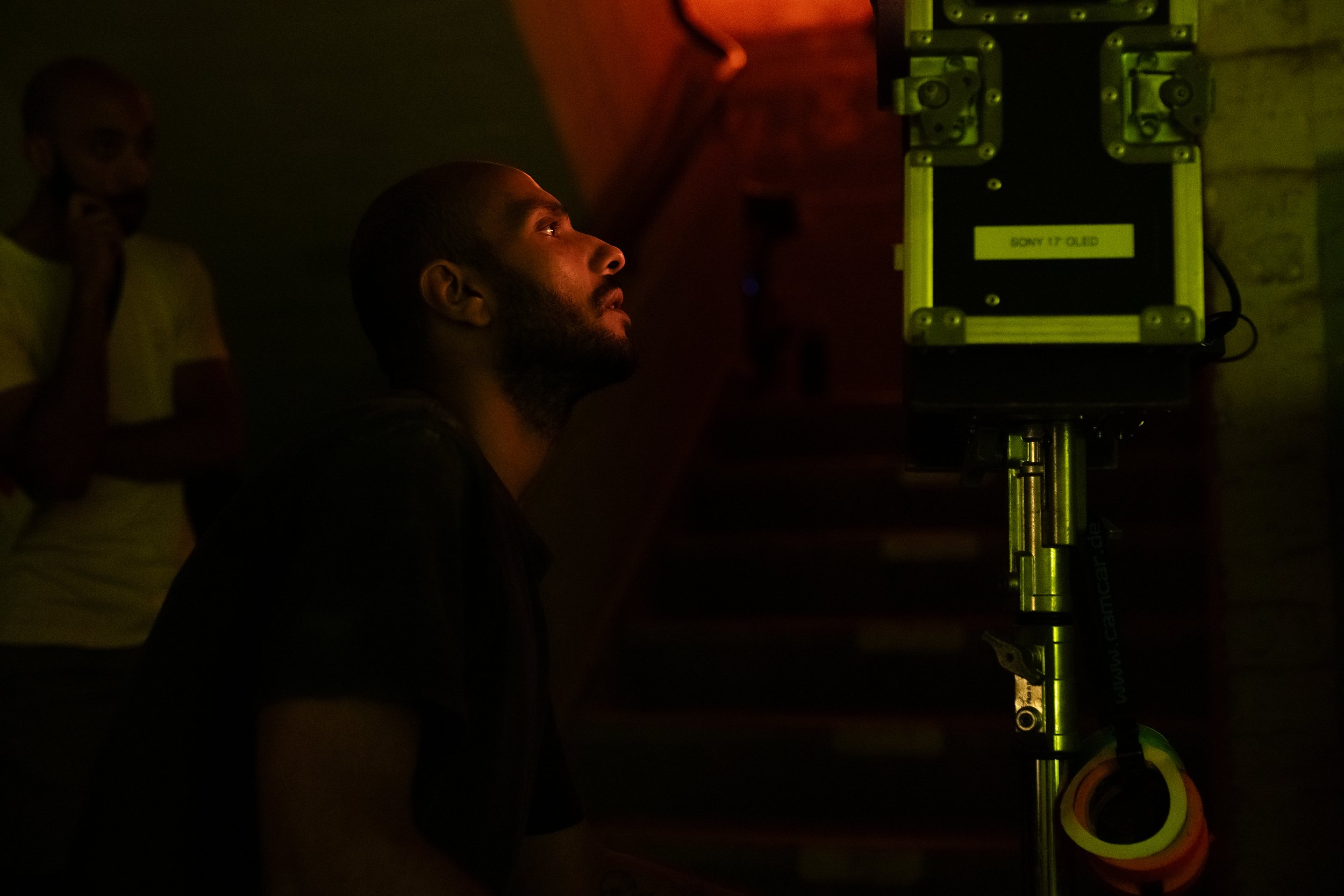 Drei Männer in dunklem Raum, einer sitzt vor einem Bildschirm, während die anderen stehen, der Bildschirm trägt ein Etikett mit 'SONY 17 OLED'.