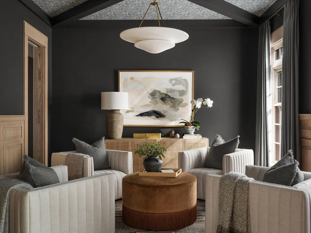 Living room with dark gray walls, light-colored furniture, a large abstract painting, a wooden sideboard, and a chandelier.