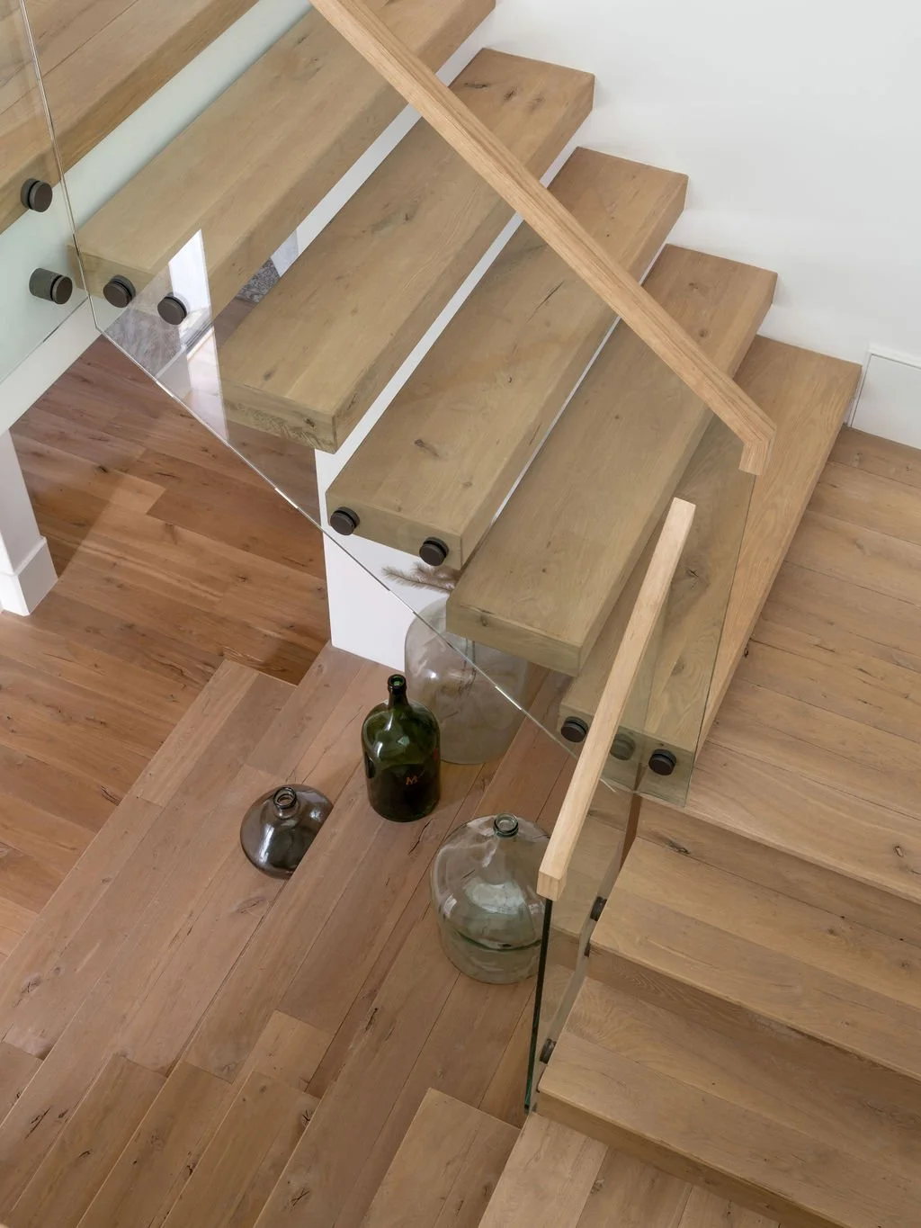Top-down view of wooden stairs with glass railing, decorated with empty glass bottles placed on the steps.
