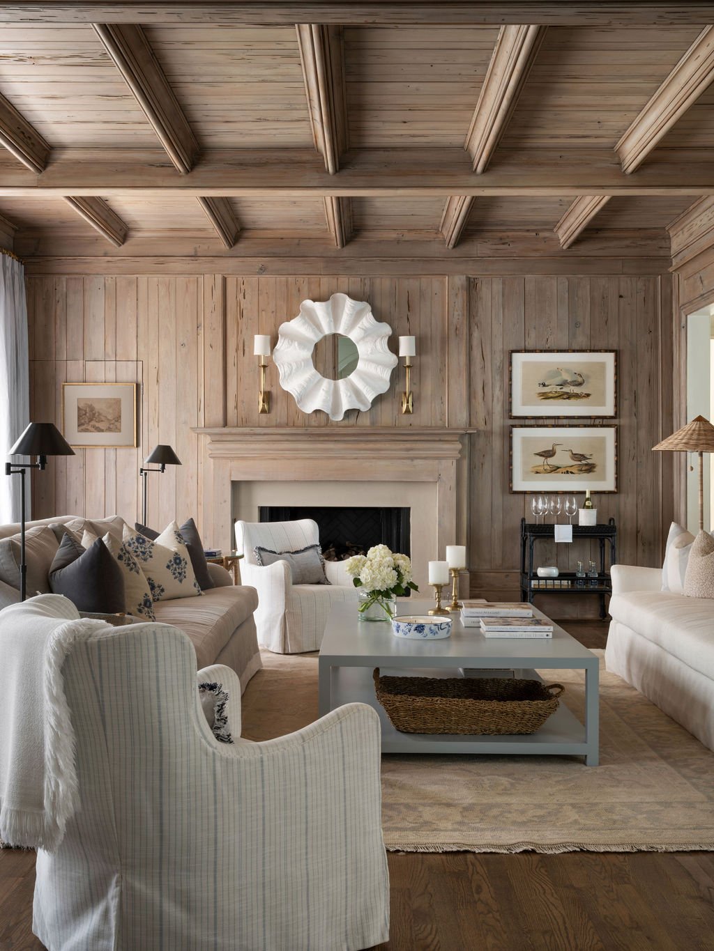 Living room with wood-paneled walls and ceiling, white sofas, armchairs, and a coffee table with flowers and candles.