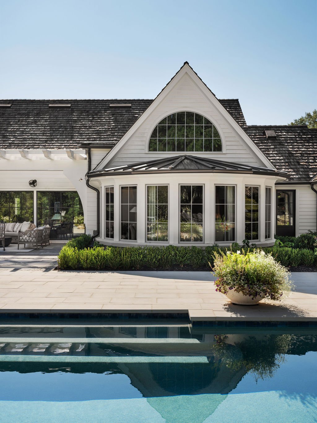 A modern white house with large windows, a triangular roof, and a swimming pool in the foreground.