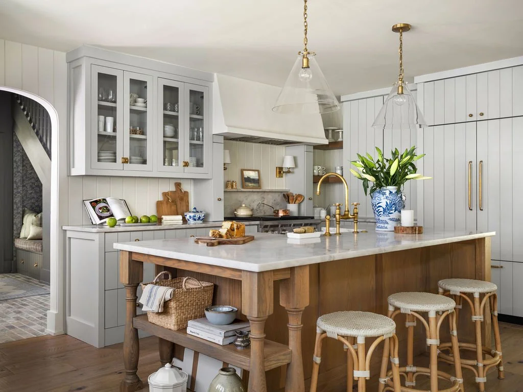Modern kitchen with white cabinetry, a marble island, brass fixtures, and rattan bar stools.