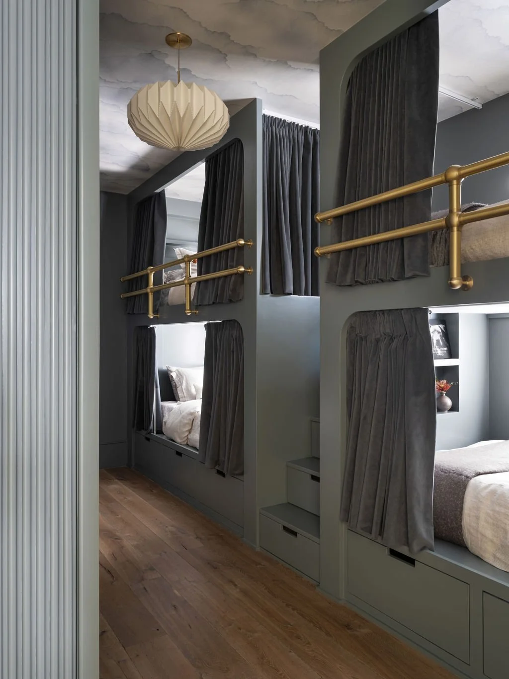 Interior of a modern bedroom with built-in beds and small private spaces separated by curtains, featuring gold-colored guardrails and wooden flooring.