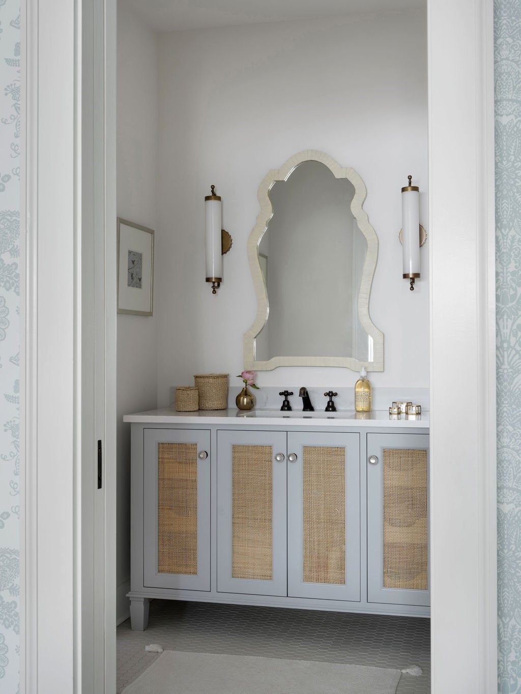 A bathroom vanity with a light blue cabinet, cane panel doors, and a white countertop, a mirror above, and two wall-mounted lights on either side.
