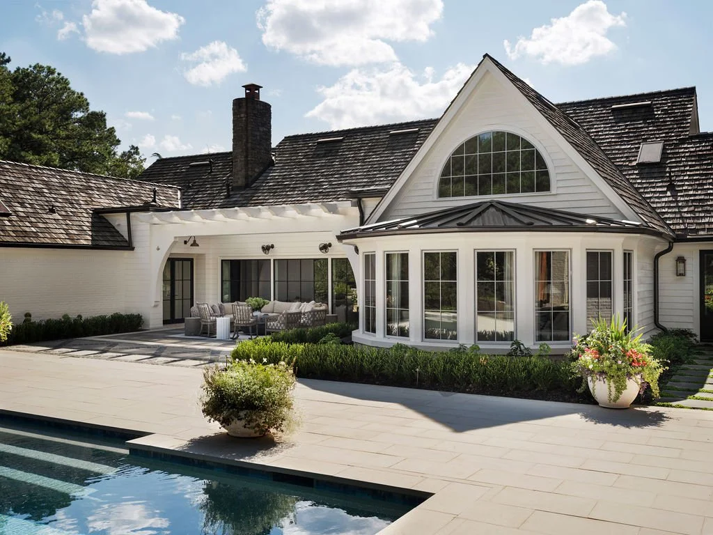 Luxury house with large glass windows, patio patio furniture, and a swimming pool in the backyard on a sunny day.