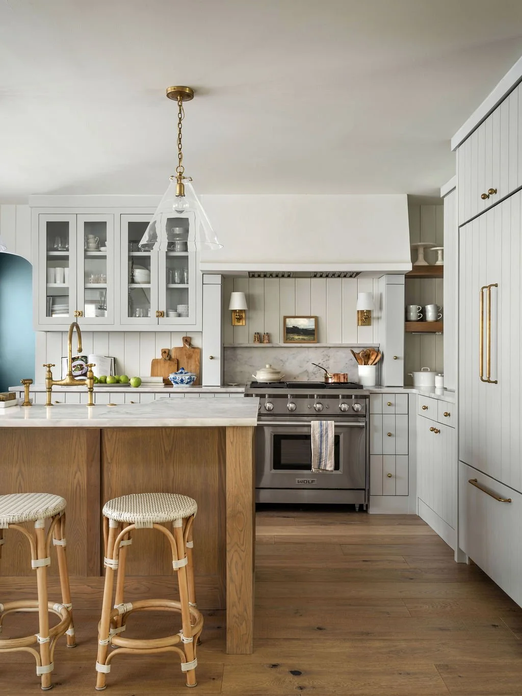 A kitchen with white cabinets, a wooden island with bar stools, and a stainless steel stove, with open shelving and decorative items.