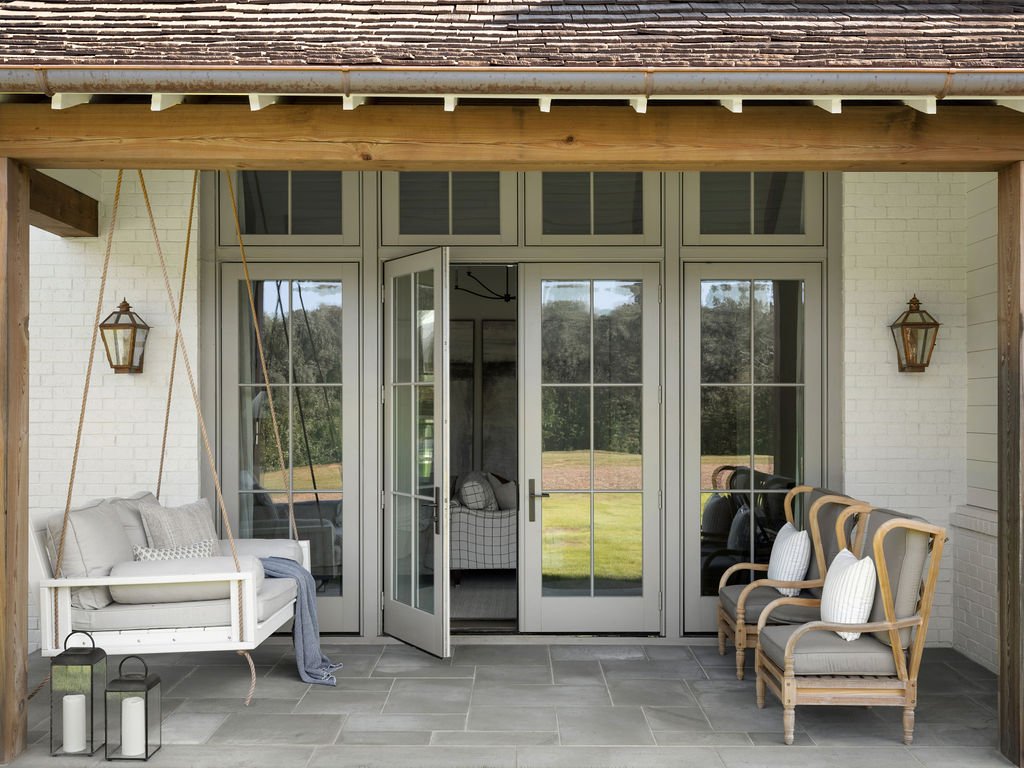 Covered porch with white swing, four wooden chairs, and decorative lanterns.