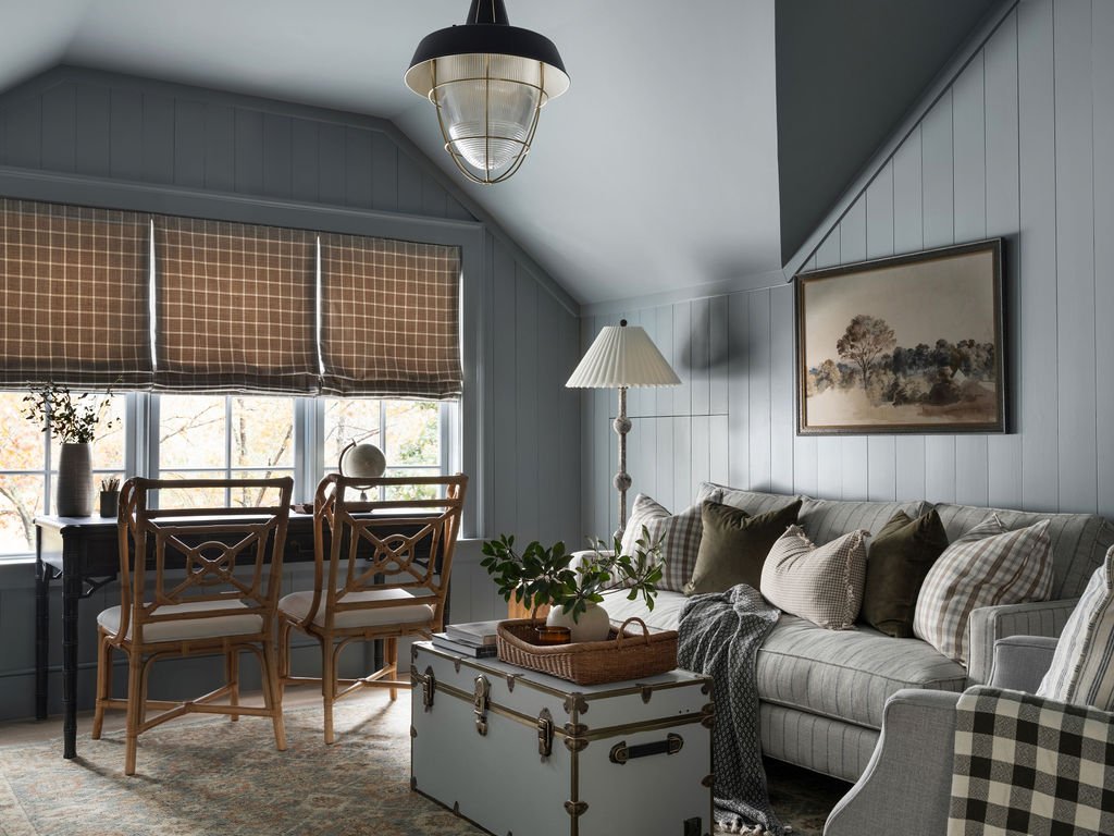 Cozy living room with a striped sofa, throw pillows, a wooden coffee table, and a framed painting on the wall. A tall floor lamp and a window with brown checkered blinds are also visible.