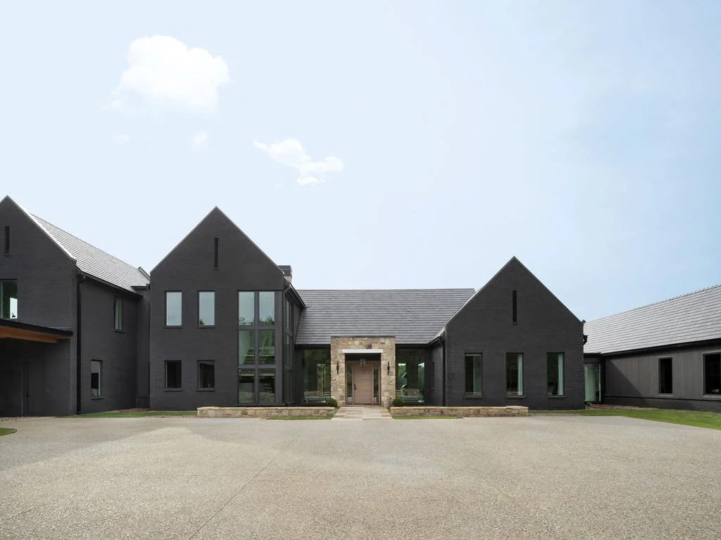Modern black house with unique steep gable roof design and large windows, exterior shot with gravel driveway and minimal landscaping.
