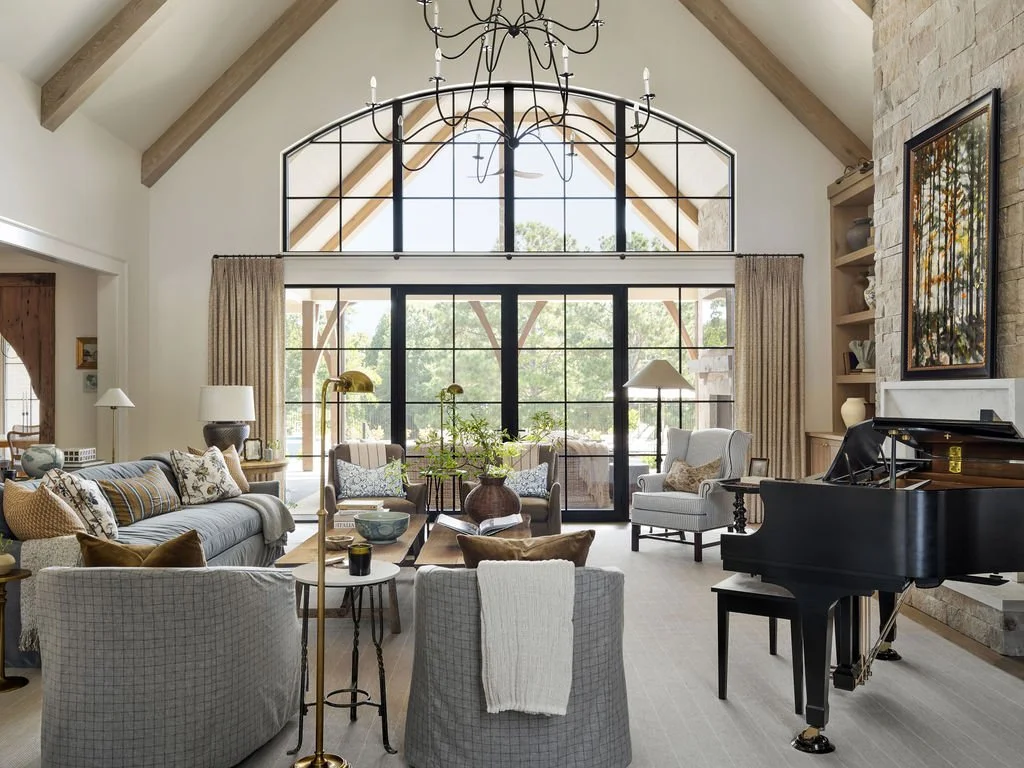 Bright living room with high vaulted ceiling, large windows, and a black grand piano.