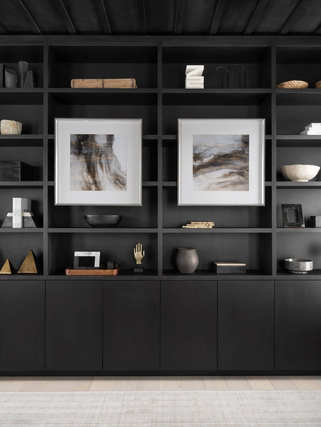 A black wall unit with shelves displaying abstract art, decorative objects, and books.