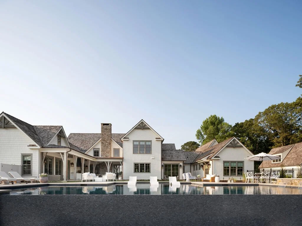 Luxury house with a swimming pool in the backyard, outdoor furniture, and umbrellas under a clear sky.