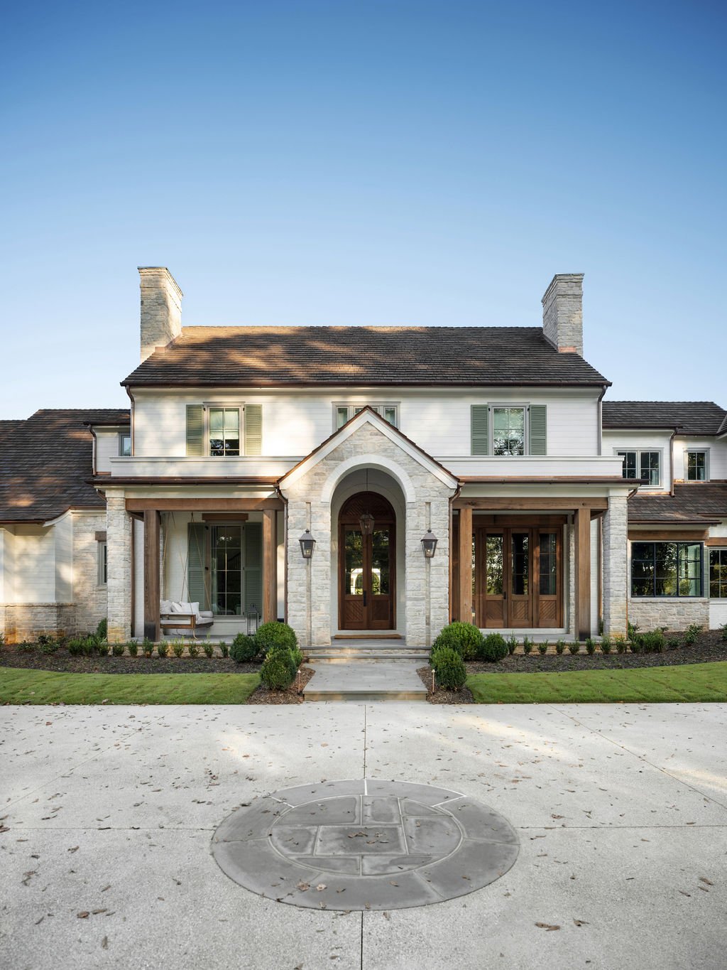 Front view of a two-story house with white siding, stone accents, brown shutters, and a gabled roof, with a concrete driveway and landscaped lawn.