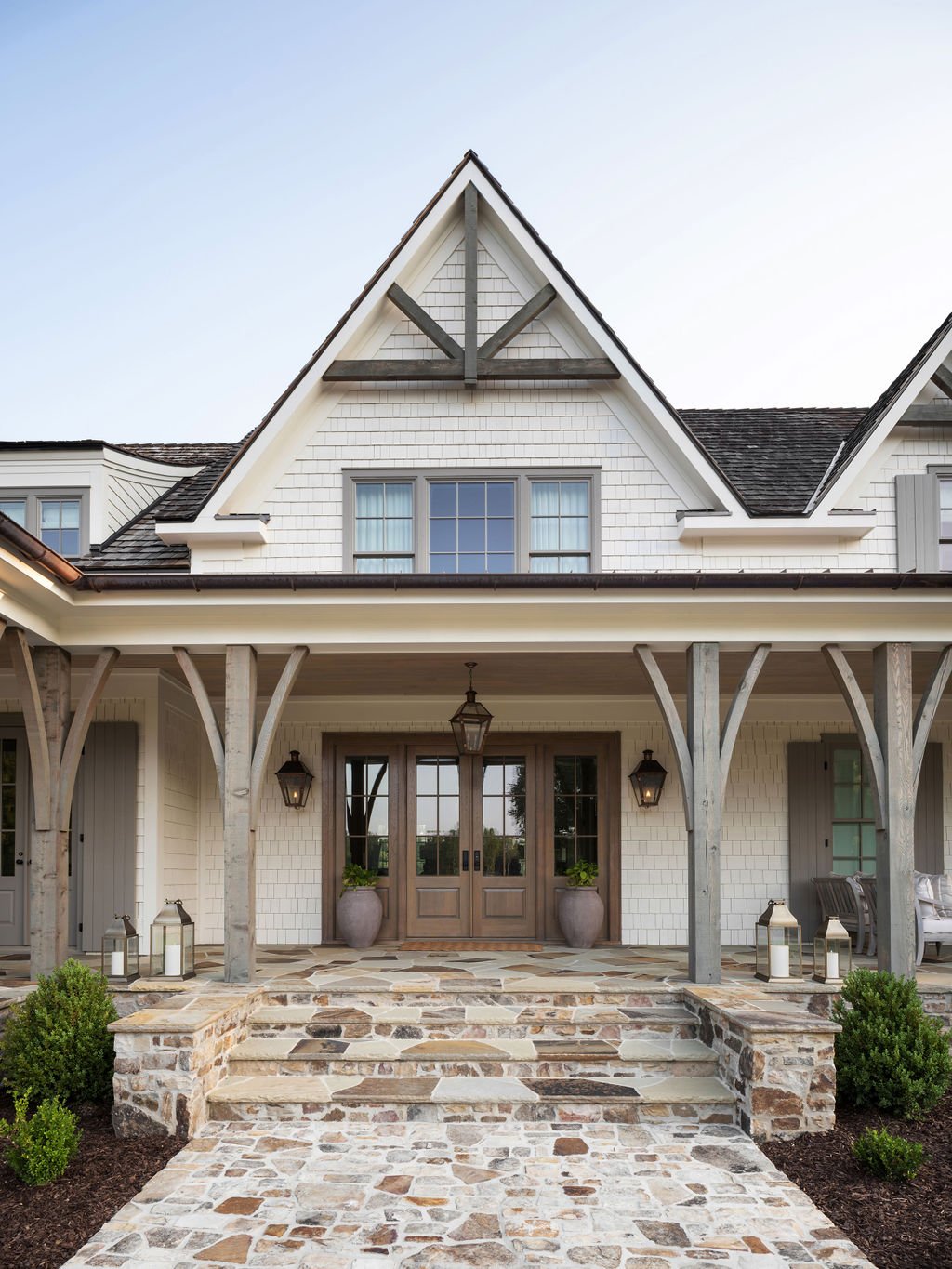 Front view of a white house with a porch, stone pathway, and gabled roof with black shingles.