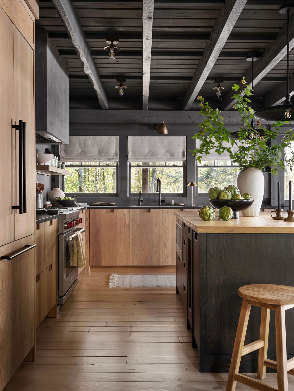 Modern kitchen with wooden cabinets, black countertops, large windows, and a kitchen island with a large vase of greenery and artichokes.