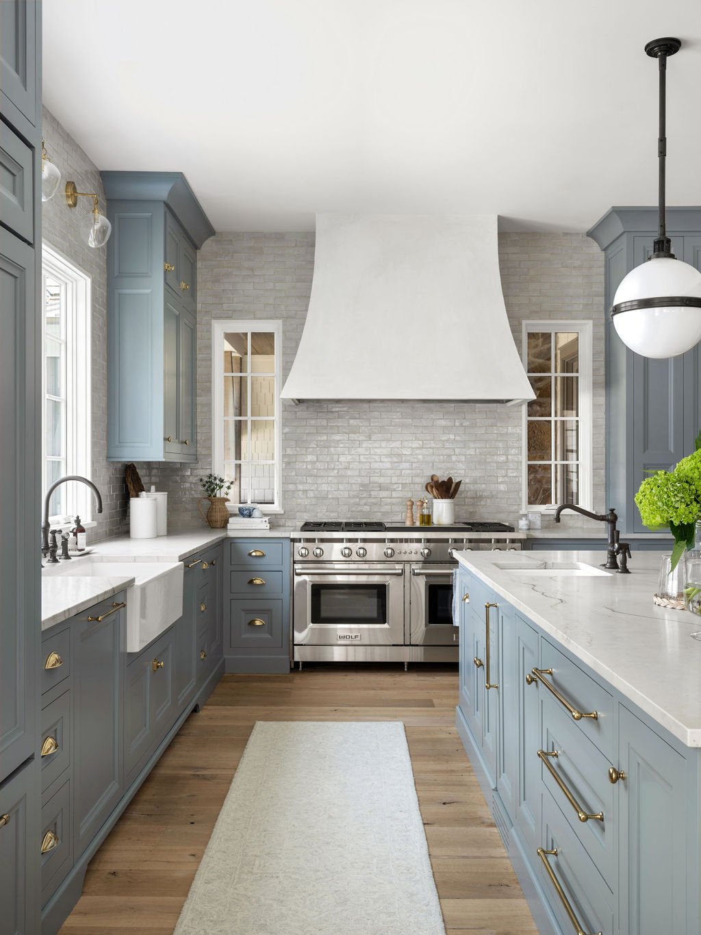 Modern kitchen with light blue cabinets, white countertops, stainless steel stove, white brick backsplash, and wooden flooring.