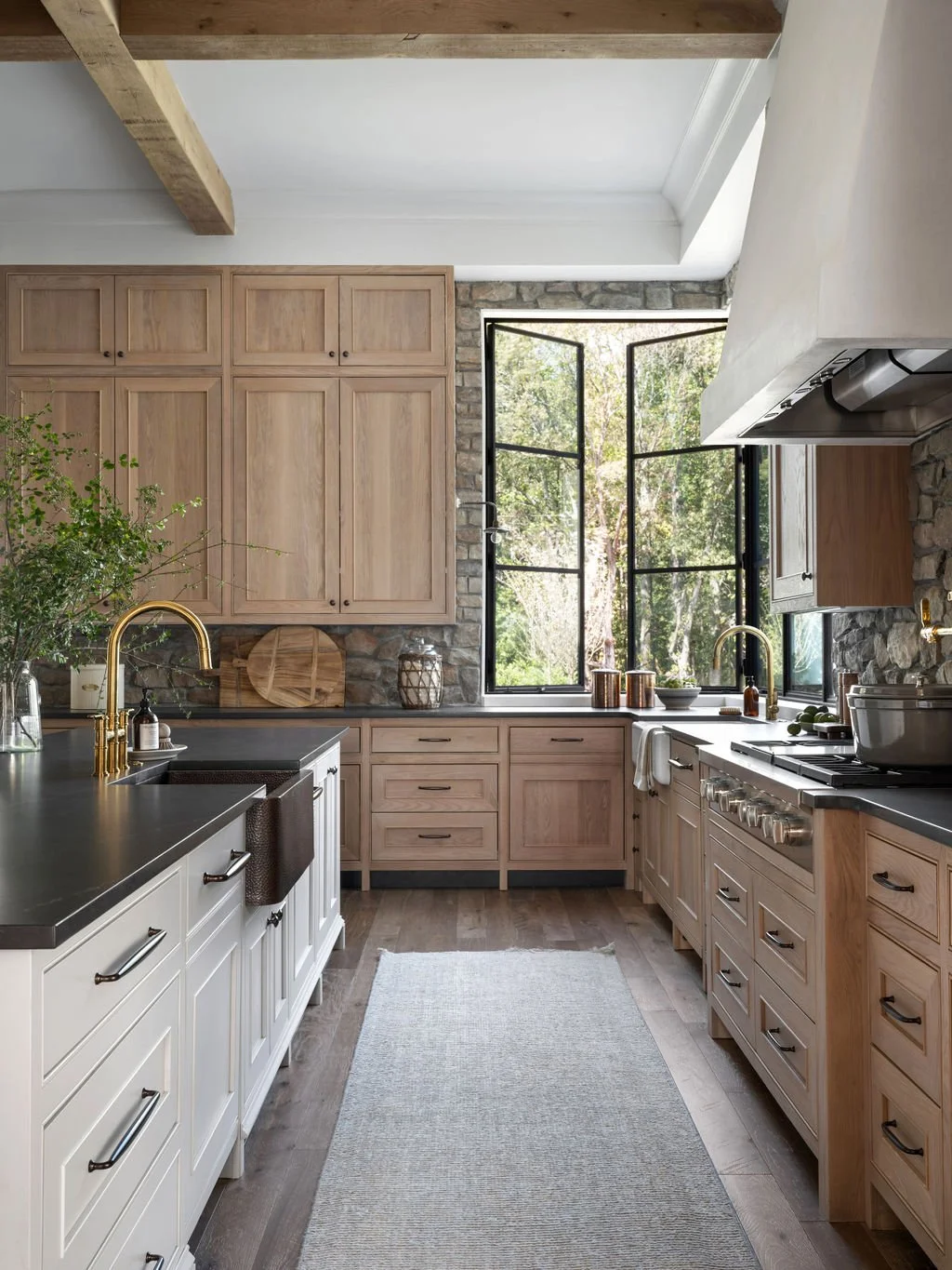 Kitchen with natural wood cabinets, black countertops, and a large open window revealing outdoor trees and greenery.