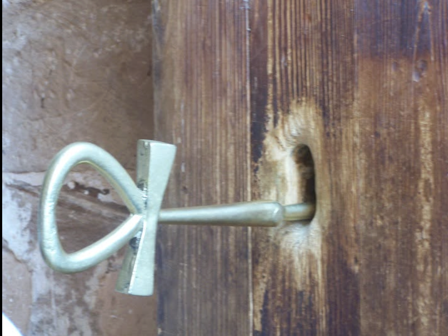 Metal nail partially hammered into a wooden surface with a heart-shaped handle.