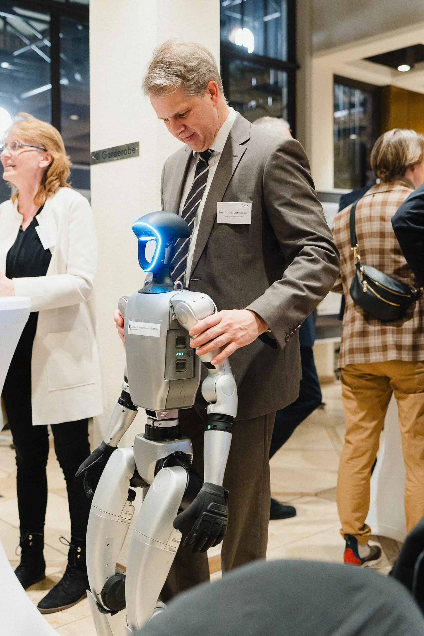 Ein Mann in Anzug und Krawatte hält einen humanoiden Roboter, der im Rahmen einer Veranstaltung oder Messe gezeigt wird.