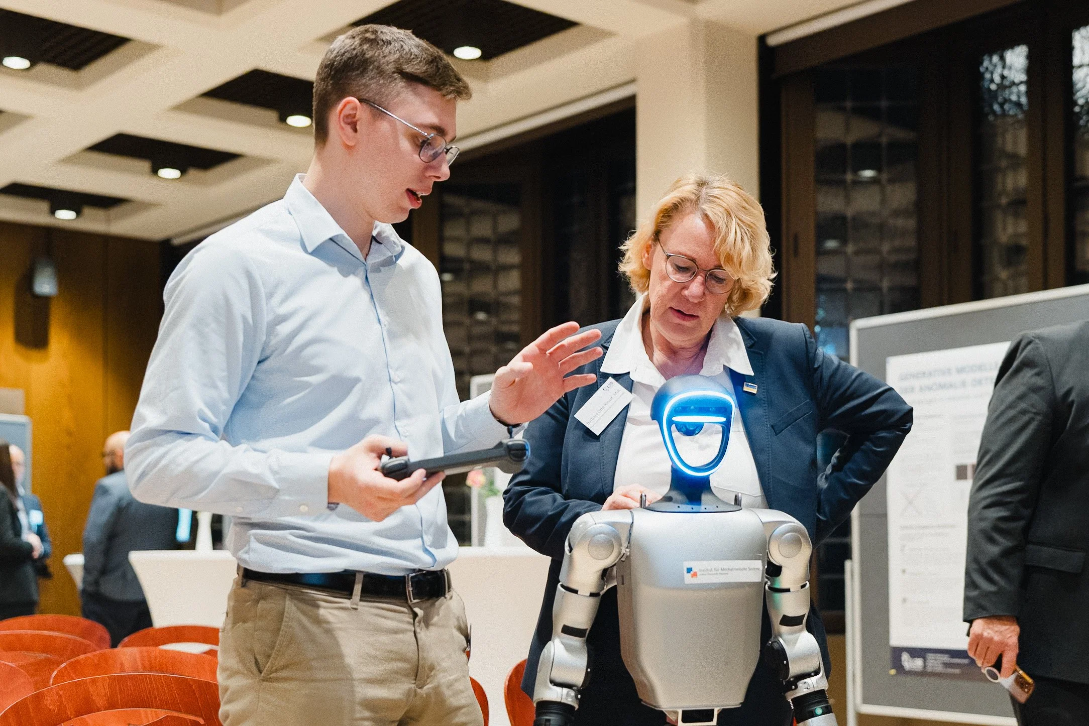 Zwei Menschen diskutieren mit einem humanoiden Roboter bei einer wissenschaftlichen Veranstaltung.