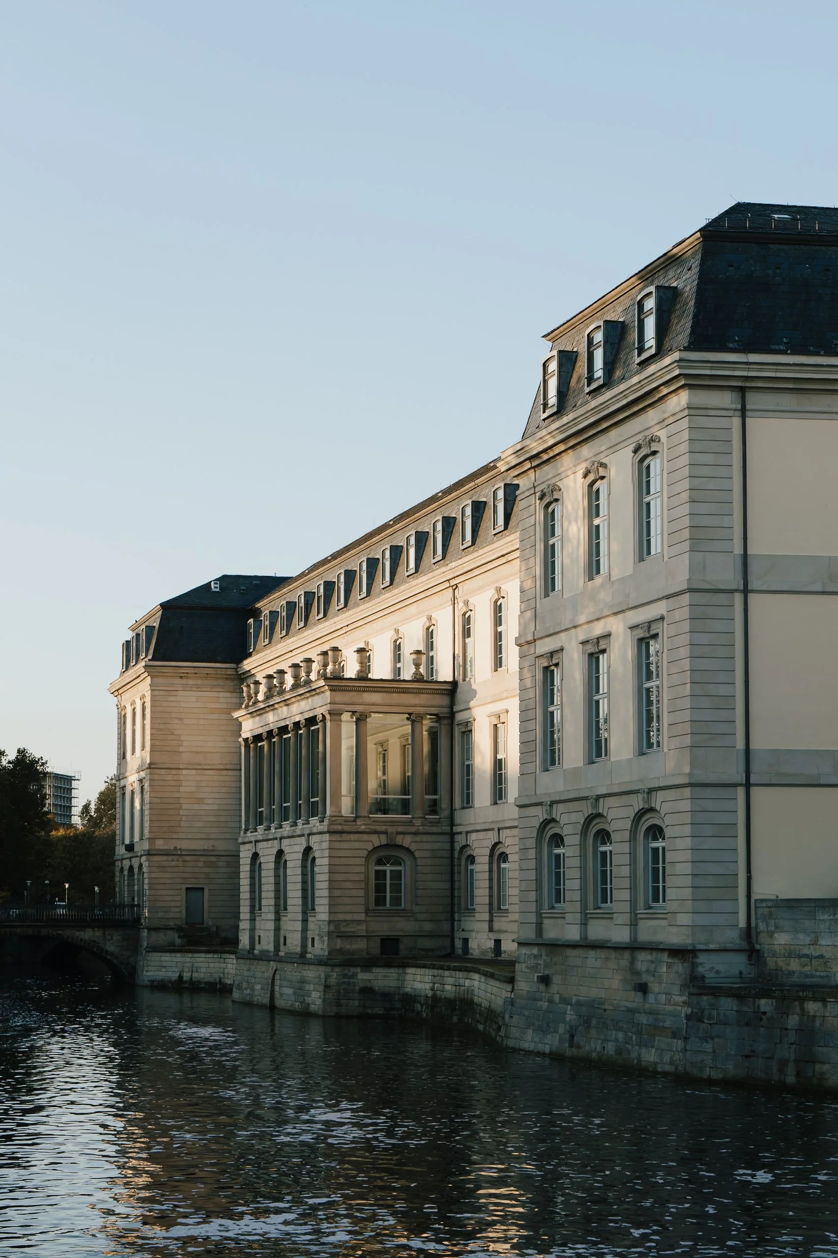 Historisches Gebäude am Wasser bei Sonnenuntergang, mit neoklassischer Architektur und vielen Fenstern.