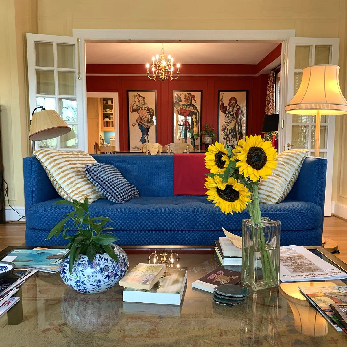 living room with blue couch, red walls in next room and sunflowers in foreground