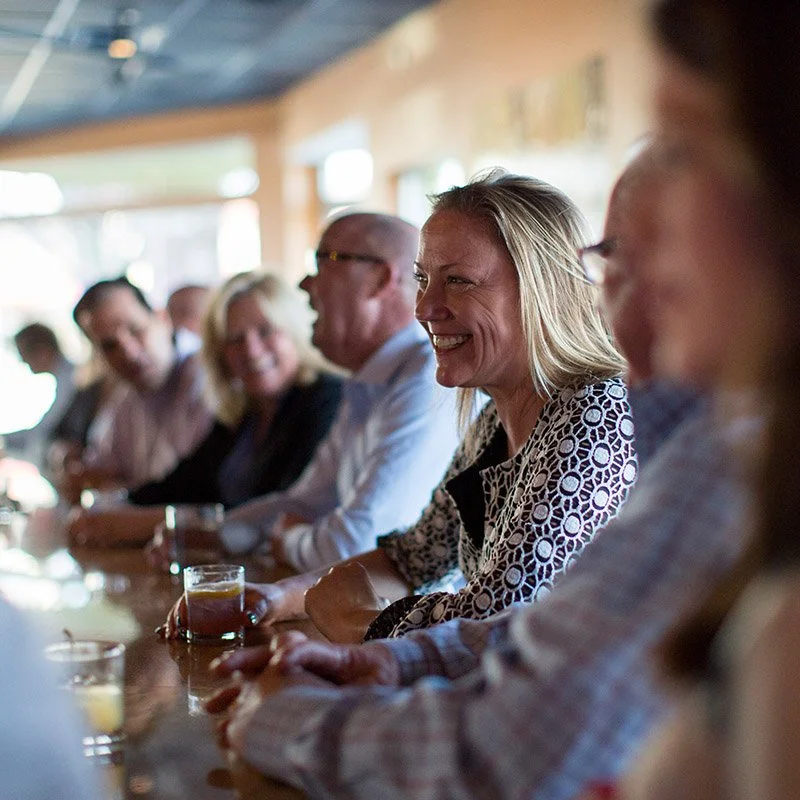 Group of people sitting at a bar or counter, smiling and engaging in conversation, with drinks in front of them.