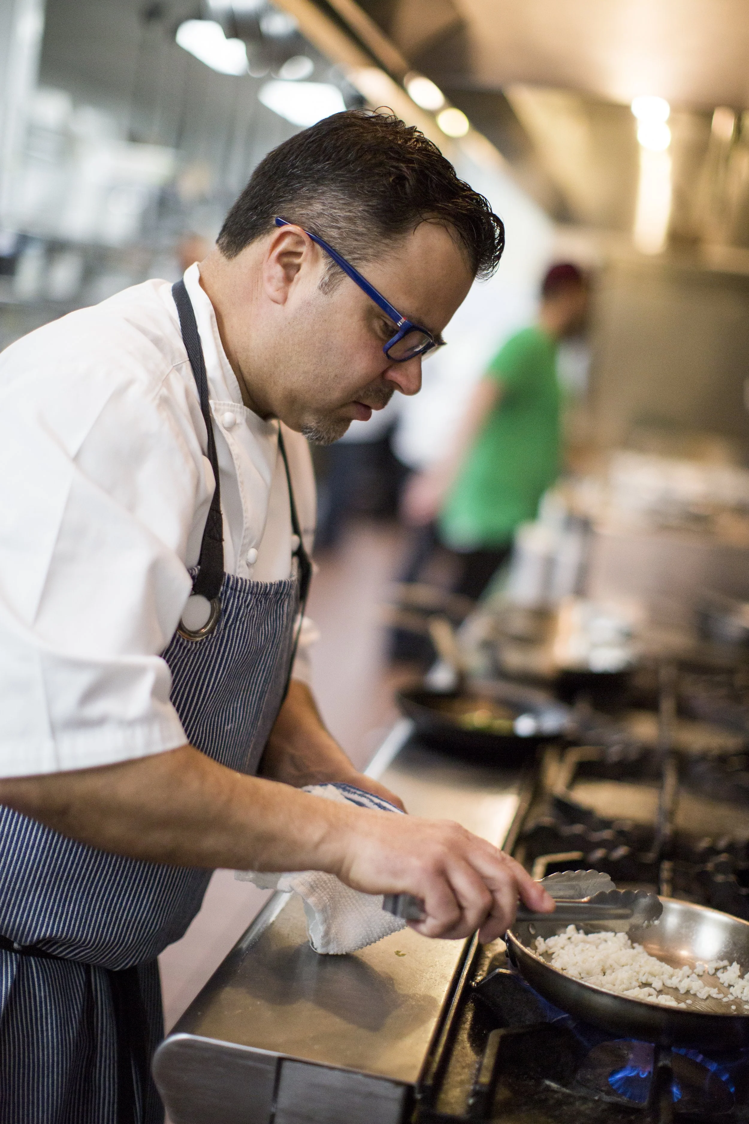 Chef preparing rice in a frying pan on a stove in a professional kitchen.