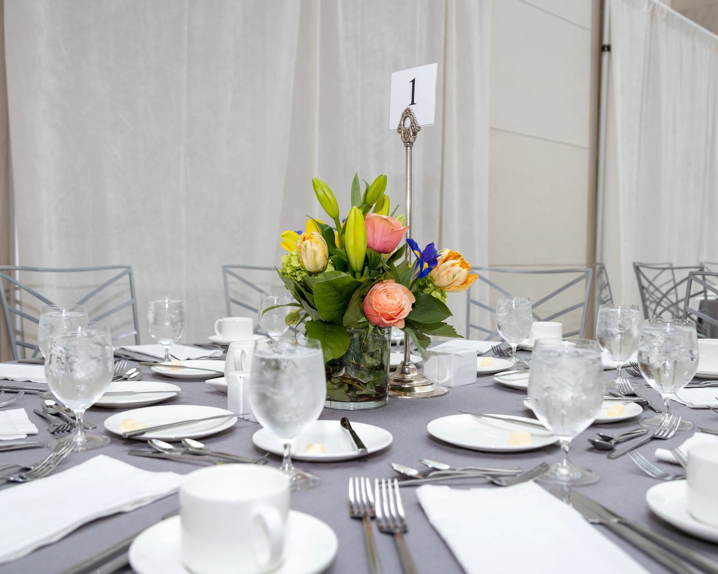A table set for a formal event with a floral centerpiece and multiple glasses and plates, numbered table sign.