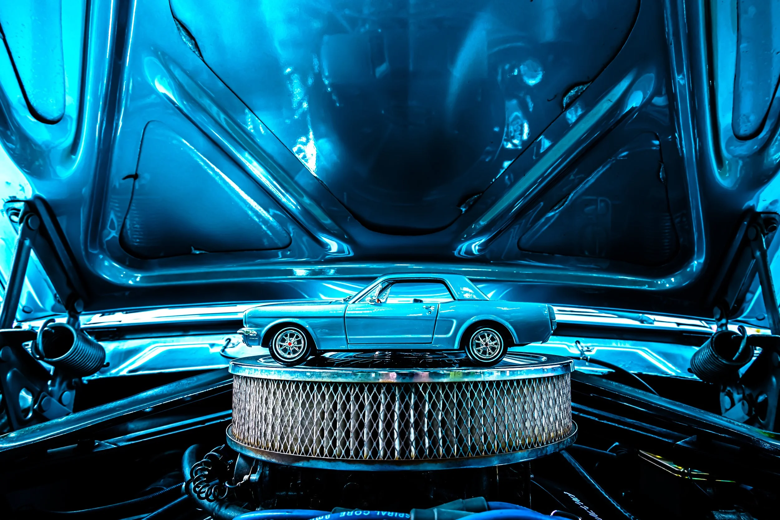 Close-up view of a vintage blue car model on a pedestal inside a shiny, futuristic engine bay with blue lighting.