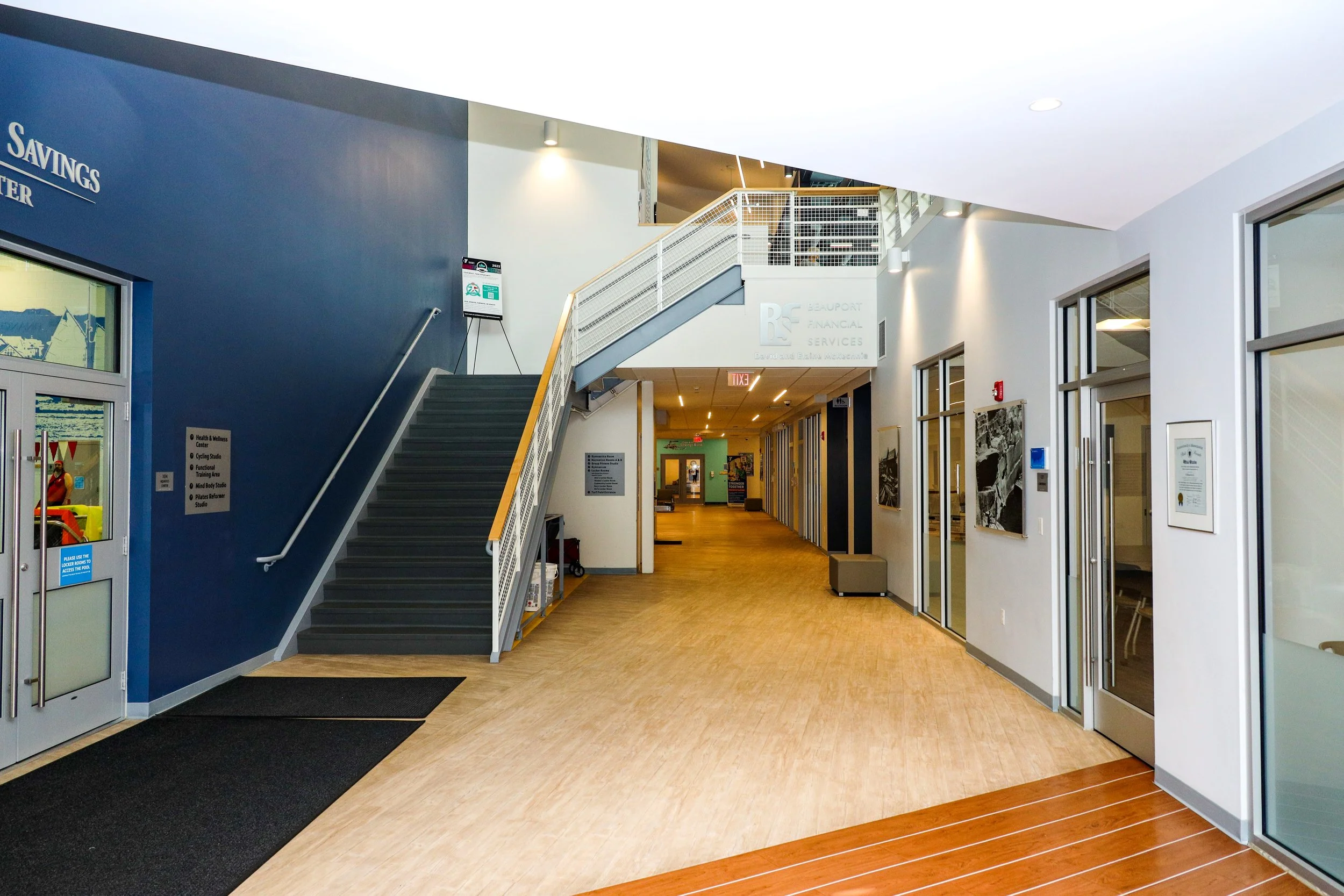 Interior view of a modern office or community center with a staircase on the left, artwork on the walls, and doors leading to different rooms on the right.