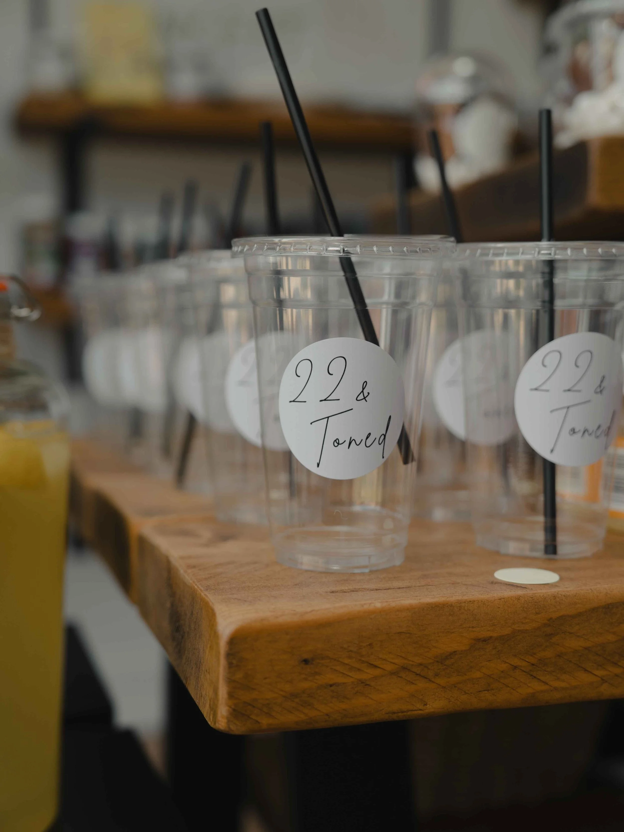 Clear plastic cups with black straws on a wooden surface, labeled '22 & Toned'