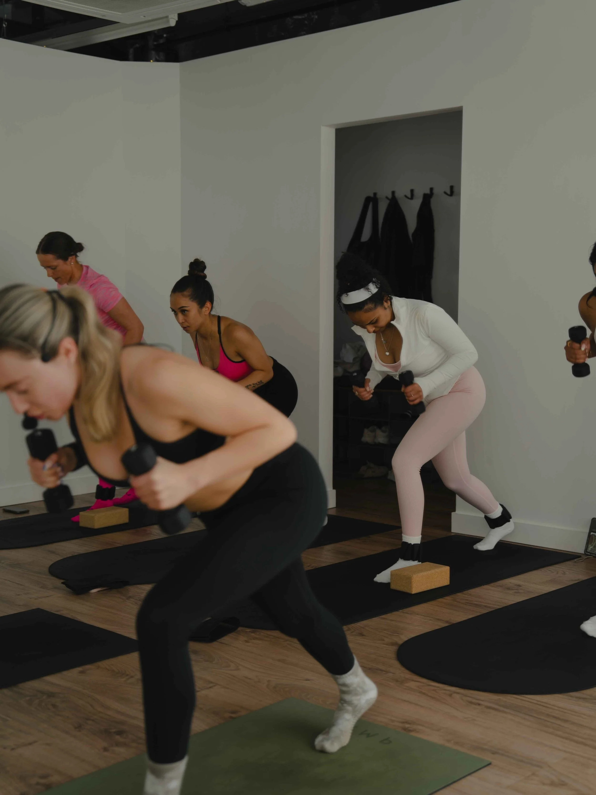 Women participating in a fitness class using dumbbells on yoga mats in a studio.