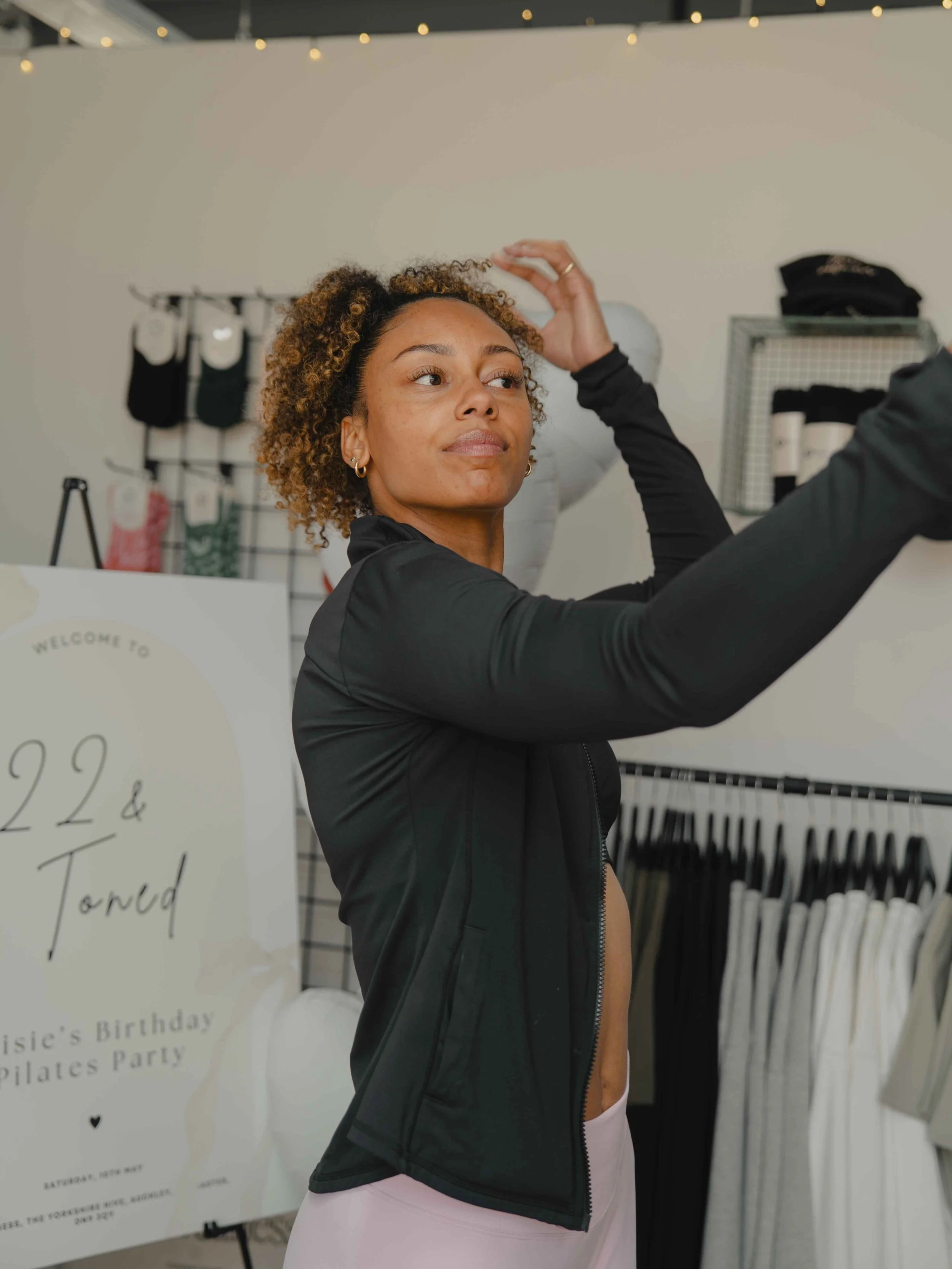 A woman adjusting her hair in a store, with a birthday invitation board in the background.