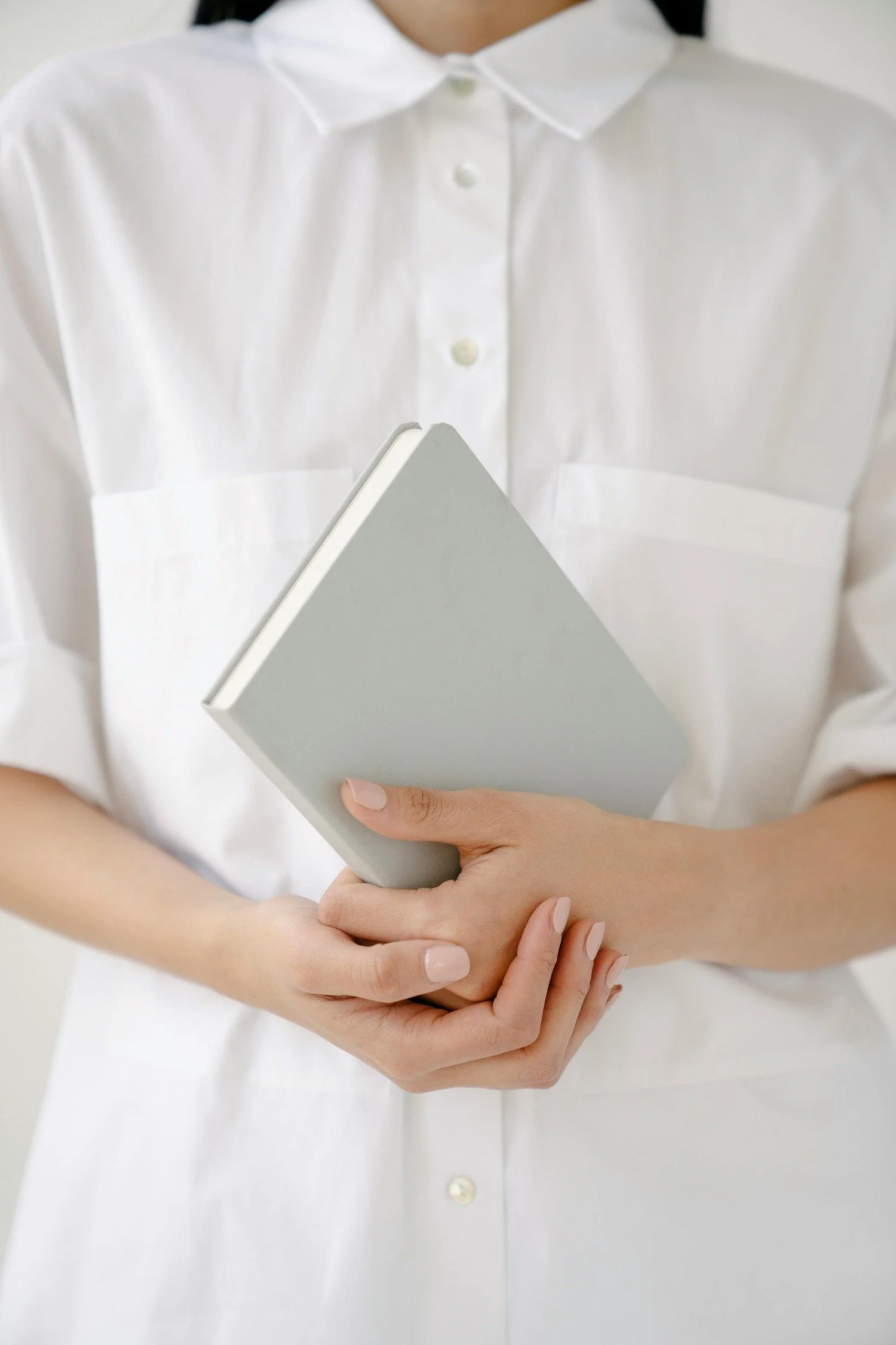 Person wearing a white button-up shirt holding a closed light gray notebook.