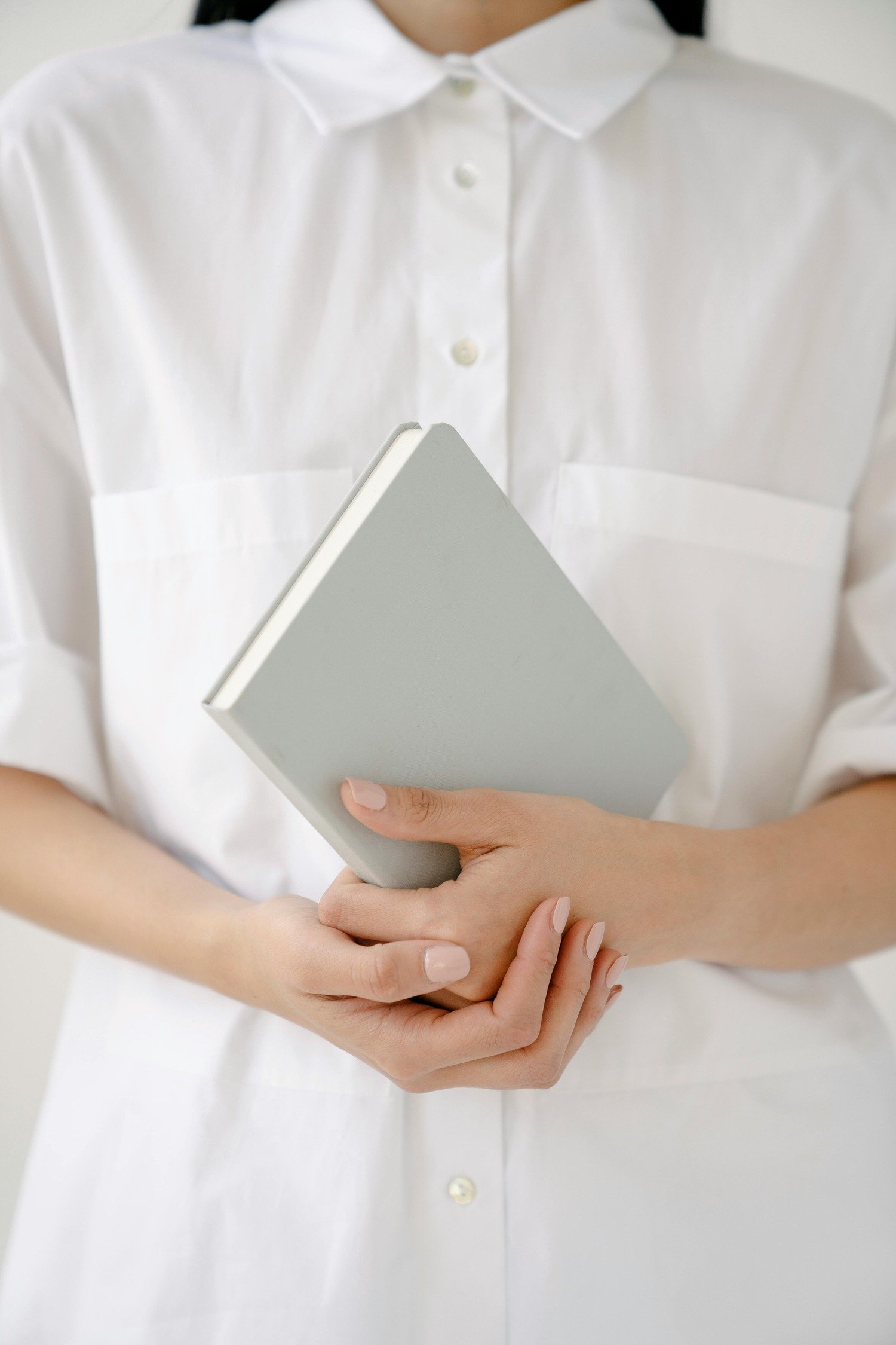 Person in a white shirt holding a closed pale gray book or notebook.