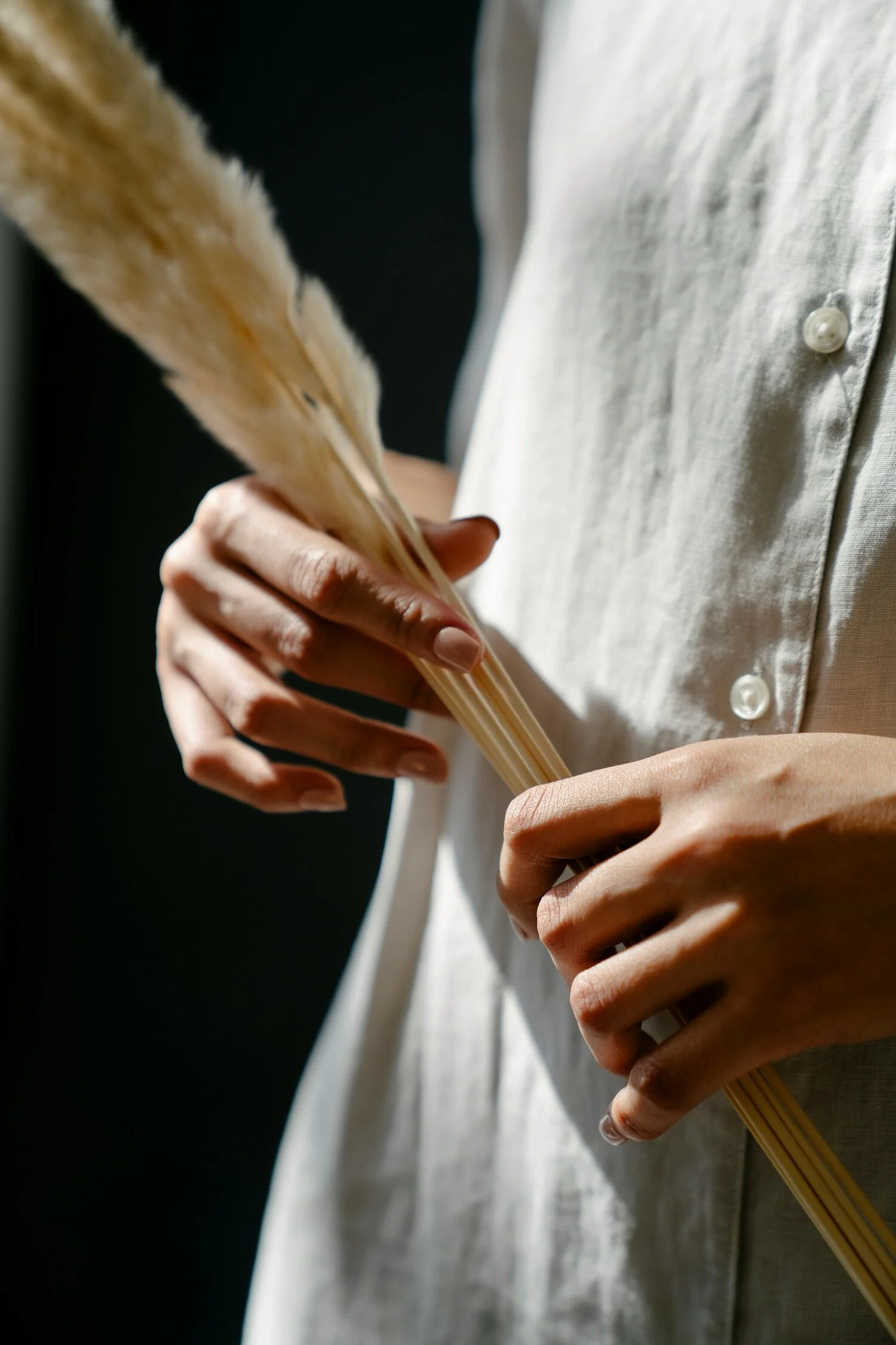 Close-up of a person holding a bundle of dried pampas grass in their hands, wearing a white shirt with buttons.