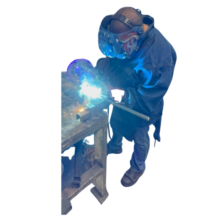 A person welding metal on a workbench, wearing a welding helmet and protective clothing.